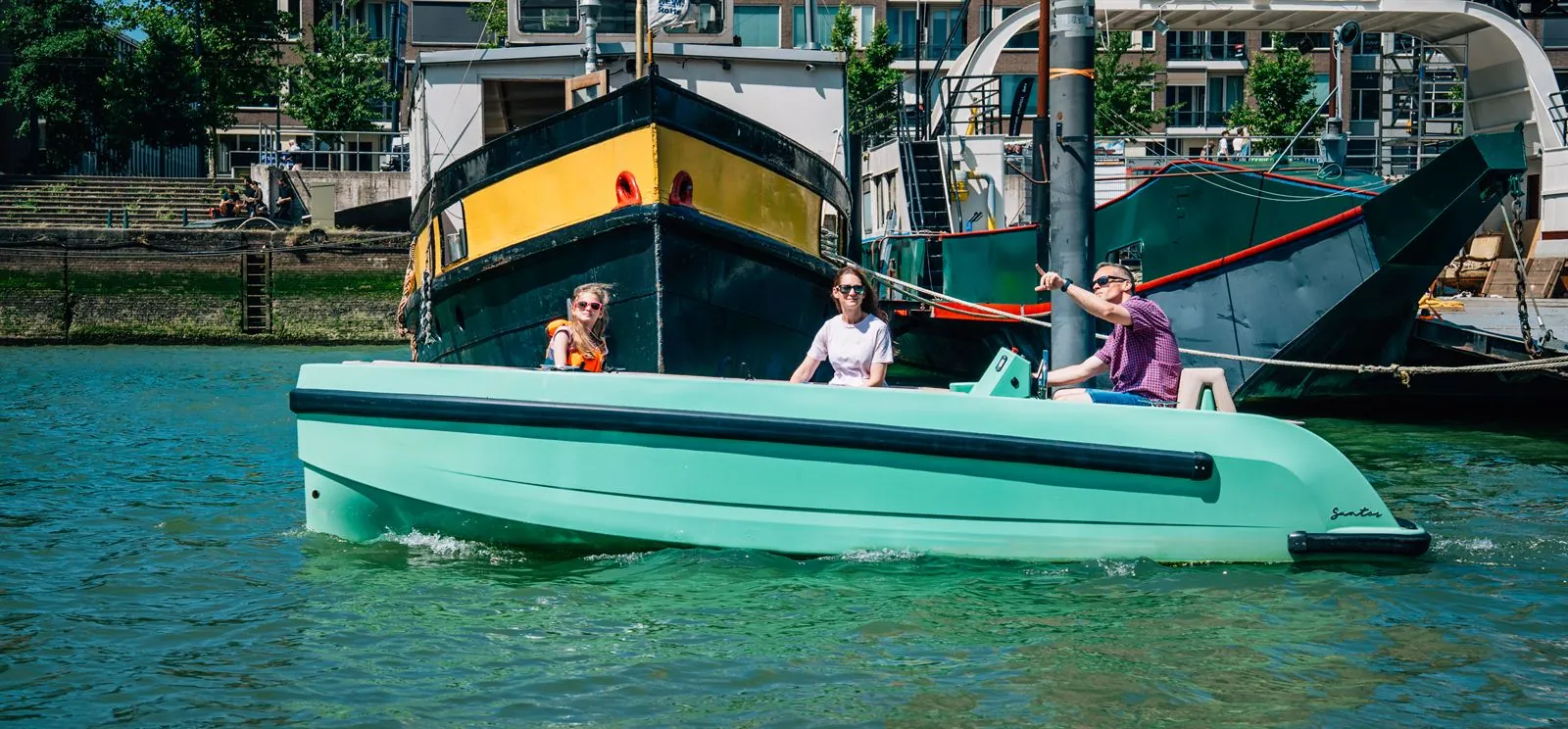 De mintgroene elektrische Santos-sloep vaart met opvarenden door de Oude Haven, historische schepen op de achtergrond